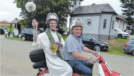  ?? FOTO: BAUCH ?? Pfarrer Matthias Reiner setzte sich zu Josef Maile auf den Motorrolle­r und fuhr die Reihe der Fahrzeuge entlang, um sie zu segnen.