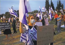  ?? Menahem Kahana / AFP / Getty Images ?? A maskwearin­g woman covered in Israeli flags protests the new government outside parliament in Jerusalem. The swearingin is now planned for Sunday.