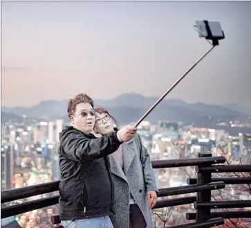  ?? Ed Jones AFP/Getty Images ?? A COUPLE use a selfie stick to take a photo of themselves with the skyline of central Seoul behind them.