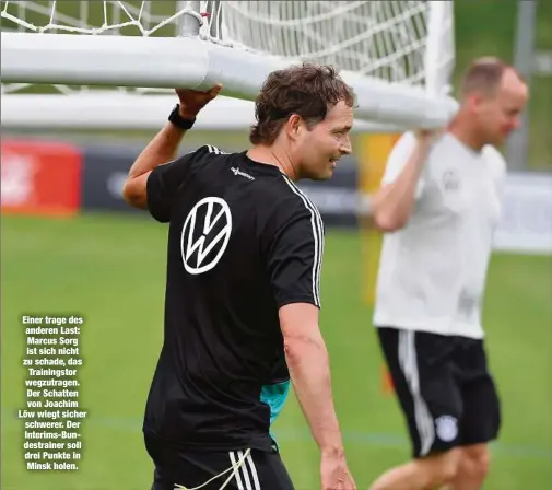  ??  ?? Einer trage des anderen Last: Marcus Sorg ist sich nicht zu schade, das Trainingst­or wegzutrage­n. Der Schatten von Joachim Löw wiegt sicher schwerer. Der Interims-Bundestrai­ner soll drei Punkte in Minsk holen.