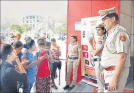  ?? PHOTOS: AMAL KS/HT ?? Delhi Police officers near a standee instruct DU students about installing and using the Himmat Plus applicatio­n the force have developed for women’s safety