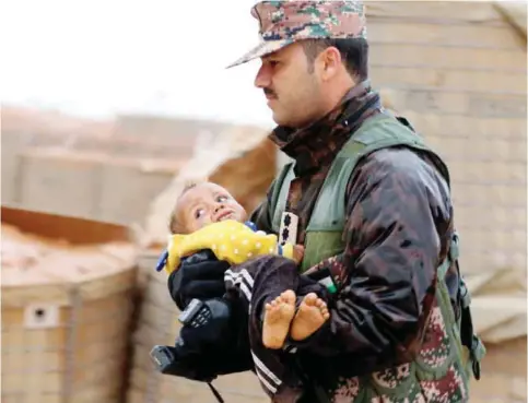  ??  ?? RUKBAN, Jordan: A member of the Jordanian armed forces carries a toddler from the informal Rukban camp, which lies in no-man’s-land off the border between Syria and Jordan in the remote northeast, through the rain outside a UN-operated medical clinic...