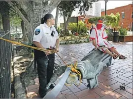  ?? Gary Coronado Los Angeles Times ?? AN ACTIVIST SITS atop a felled statue Saturday in downtown Los Angeles’ Father Serra Park, where a monument to Father Junipero Serra was torn down.