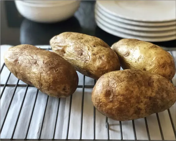  ?? ELIZABETH KARMEL VIA AP ?? This photo shows four baked potatoes resting on a rack in Amagansett, N.Y. Preheat the oven to 350degrees Fahrenheit and place a sheet of heavy-duty aluminum foil on the bottom shelf of the oven in case any of the juices drip. After washing and drying the potatoes, coat them with either a little regular Crisco shortening or olive oil. Then prick them four or five times with a fork to let steam escape while they are baking. After an hour of baking, stick the end of a paring knife into the potato to gauge its doneness. It generally takes another 20 minutes to be perfect, but it depends on the potato’s size.