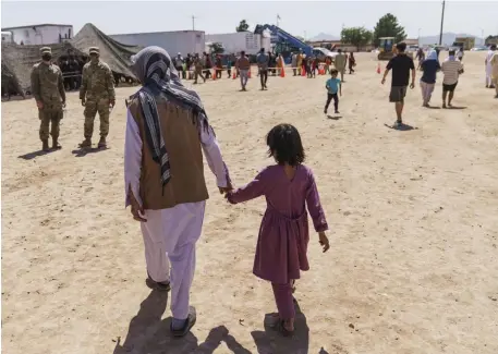  ?? Ap File pHotoS ?? WAITING ON A NEW HOME: A man walks with a child through Fort Bliss’ Dona Ana Village, where Afghan evacuees are being housed, in New Mexico, Sept. 10. Below, evacuees line up for food.