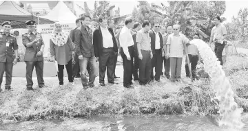  ??  ?? Uggah (front right) and other officials checking on the water flowing from the tube well in front of the Tudan watchtower yesterday.