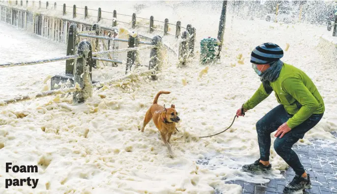  ?? Picture: EPA-EFE ?? A man walks his dog through thick sea foam blowing ashore during a storm in Seapoint, Cape Town, yesterday. The third in a succession of powerful cold fronts have swept over the peninsula, causing extensive damage. Waves in excess of 10m have been crashing into the Cape’s west coast with gale force winds and flooding.