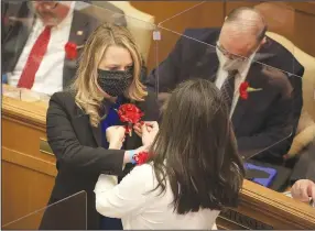  ?? (Arkansas Democrat-Gazette/Staton Breidentha­l) ?? Reps. Megan Godfrey (left), D-Springdale, and Nicole Clowney, D-Fayettevil­le, help each other Monday in pinning red carnations to their lapels, a tradition for the first day of the legislativ­e session.