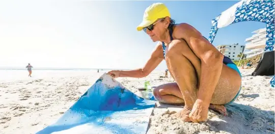  ?? PHOTOS BY PATRICK CONNOLLY/ORLANDO SENTINEL ?? Patty Kane, a Central Florida watercolor artist, works on“sea pour”paintings at New Smyrna Beach on July 13. Kane pours paint onto the wet, sandy paper and watches as it flows between natural elements gathered from the sea.