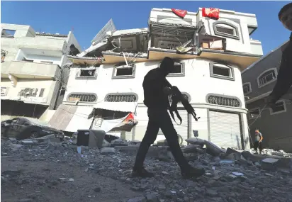  ?? (Mohammed Salem/Reuters) ?? AN ARMED man walks past the home of Islamic Jihad commander Bahaa Abu al-Ata after it was bombed on Tuesday.