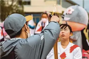  ?? AFP PIC ?? An official (left) prepares to transfer the Olympic flame from the torch, Momomi Kodama is holding, to a lantern at Tomioka Daiichi Junior High School during the first day of Tokyo 2020 Olympic Games torch relay in Tomioka, Fukushima yesterday.