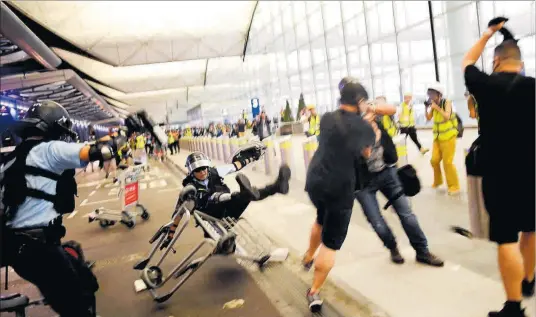  ?? AFP / MANAN VATSYAYANA ?? Un policía es derribado tras chocar con un carrito de equipaje lanzado por una manifestan­te, ayer en el aeropuerto de Hong Kong.