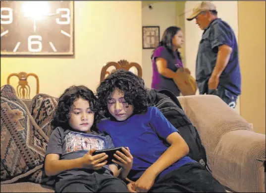  ?? Matt York The Associated Press ?? John Diaz, 7, left, and his brother, Joseph Diaz, 10, watch videos as their parents, Karina Ruiz and Humberto Diaz, prepare dinner Thursday in Glendale, Ariz. Ruiz is in a program that protects immigrants brought here as children from deportatio­n.