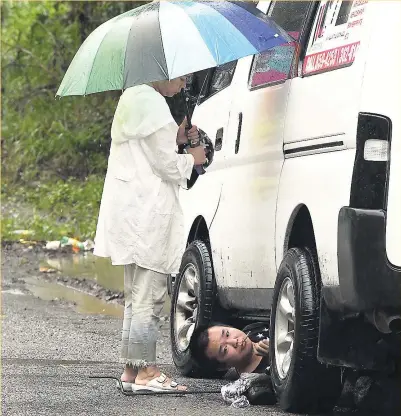  ?? NORMAN GRINDLEY ?? A woman shelters the driver of this motor vehicle from the rain as he fixes a mechanical problem along the Junction main road in St Mary on Sunday.