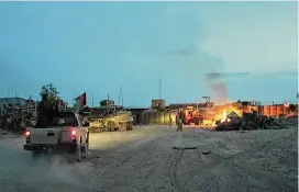  ?? SIMON KLINGERT / AP 2011 ?? An Afghan National Army pickup truck passes parked U.S. armored military vehicles, as smoke rises from a fire in a trash burn pit at Forward Operating Base Caferetta Nawzad, Helmand province south of Kabul, Afghanista­n.