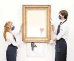  ??  ?? Art handlers at Sotheby’s auction house hold Banksy’s “Love is in the Bin,” before it returns to auction Friday in London.