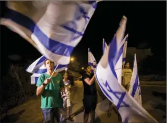  ?? TSAFRIR ABAYOV — THE ASSOCIATED PRESS ?? Israelis wave flags in the Israeli settlement of Halamish, Saturday. Israel’s military has sent more troops to the West Bank and placed forces on high alert a day after a Palestinia­n stabbed to death three members of an Israeli family and...