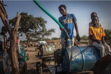  ??  ?? Young hawkers fill barrels with water in the wadis Moura in Hadjer Hadid, in the Ouaddaï region, in eastern Chad on Mar 24 and (photo left) a hawker looks on after filling barrels with water. — AFP photos