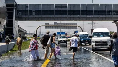  ?? ?? People walk through floodwater caused by heavy rain while waiting for transporta­tion on Sheikh Zayed Road highway in Dubai.