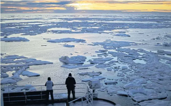  ??  ?? BROKEN ICE: Researcher­s look out from Finnish icebreaker ‘MSV Nordica’ as the sun sets over sea ice floating on the Victoria Strait along the Northwest Passage.