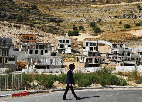  ?? (AMMAR AWAD/REUTERS) ?? Un colon juif passe devant des chantiers proches de Givat Zeev et Ramat Givat Zeev, en Cisjordani­e occupée.