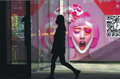  ?? WANG ZHAO/ AGENCE FRANCE-PRESSE ?? A woman walks past an advertisem­ent at the entrance of a store in Beijing last week. Stores across the city have launched promotion campaigns ahead of the Spring Festival holiday.