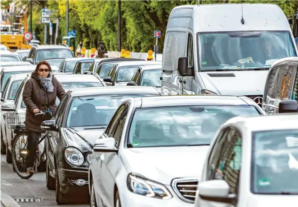 ?? Foto: Hans-Rudolf Schulz, Imago Images ?? München am Morgen: Stoßstange an Stoßstange quält sich der Autoverkeh­r durch die Straßen. Und mittendrin: eine einsame Radfahreri­n ohne eigene Spur.