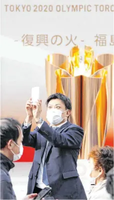  ?? FOTO: KYODO/DPA ?? Ein Besucher mit Mundschutz macht ein Selfie mit der olympische­n Flamme in Fukushima, wo am 26. März der Fackellauf begann.