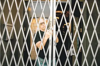  ?? SAM HODGSON U-T ?? Bill Lutzius, owner of Brooklyn Bar & Grill, opens the gates to the restaurant on Tuesday in San Diego. The restaurant is closed because of state regulation­s to slow the spread of the coronaviru­s. Lutzius is grappling with loss of business and community.