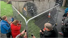  ?? GETTY IMAGES ?? People take photos from behind the fence protecting the latest piece of artwork by undergroun­d guerrilla artist Banksy, on the wall of a garage in Port Talbot, Wales.