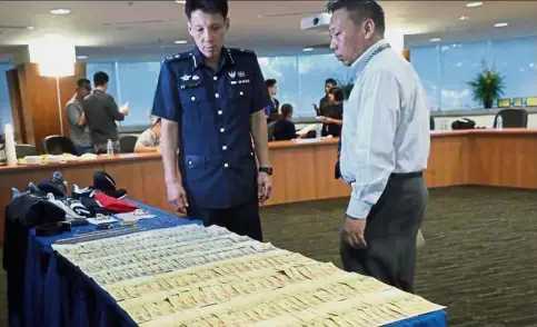  ?? — The Straits Times/Asia News Network ?? Suspicious stash: Law (left) and Inspector Ang Wee Kiat, 38, looking at the seized cash.