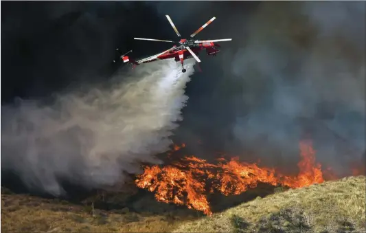  ?? Dan Watson/The Signal ?? A water-dropping helicopter makes a drop in high winds Thursday as the Tick Fire burns down a canyon and threatens homes as viewed from Stonecrest Park in Canyon Country.