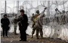  ??  ?? U.S. Customs and Border Protection agents stand watch in Tijuana as U.S. troops install wire.
