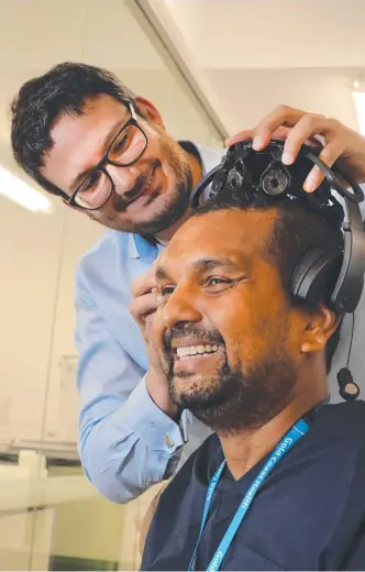  ?? Picture: GLENN HAMPSON ?? Dr Claudio Pizzolato fits a thought-control headset on Dr Dinesh Palipana.