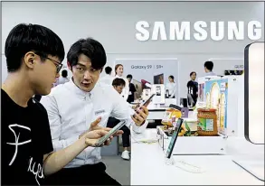  ?? Bloomberg News ?? A booth attendant (right) demonstrat­es a Samsung Electronic­s Co. smartphone to a visitor in May at the World IT Show 2018 in Seoul, South Korea. The company plans to invest in new products such as artificial intelligen­ce and 5G.