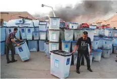  ?? AP ?? Electoral officials salvage ballot boxes as smoke rises from Baghdad’s largest ballot box storage site.