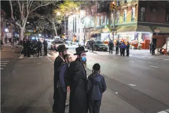  ?? Jonah Markowitz / New York Times ?? Local residents look on after police broke up a crowd of hundreds of mourners who had gathered for the funeral of a rabbi who died of the coronaviru­s in Brooklyn this week.