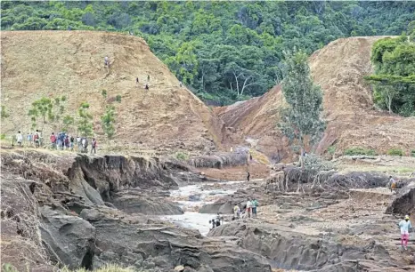  ?? Associated Press ?? People gather in front of the broken banks of the Patel dam near Solai, in Kenya’s Rift Valley, Thursday. A dam burst its banks, killing at least 44 people and forcing hundreds from their homes, officials said Thursday.