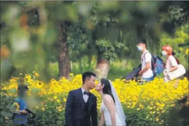  ?? ANDY WONG — ASSOCIATED PRESS ?? People wearing face masks pass by newlyweds kissing as they posing for wedding photos at the Olympic Forest Park in Beijing on July 2, 2020. Now that weddings have slowly cranked up under a patchwork of ever-shifting restrictio­ns, horror stories from vendors are rolling in. Many are desperate to work after the coronaviru­s put an abrupt end to their incomes and feel compelled to put on their masks, grab their cameras and hope for the best.