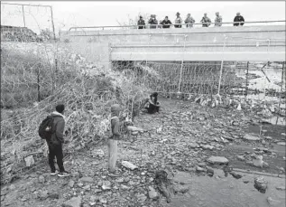  ?? John Moore Getty Images ?? LAW ENFORCEMEN­T officers and others watch migrants who had crossed the Rio Grande into Texas near Eagle Pass this week. Gov. Greg Abbott wants state authoritie­s to deport migrants.