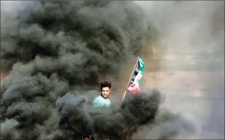  ??  ?? A Palestinia­n protester holds his national flag as smoke billows from burning tyres during a demonstrat­ion along the border with the Gaza Strip east of Gaza
City on June 1. (AFP)