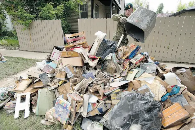  ?? JONATHAN HAYWARD/ THE CANADIAN PRESS ?? Cpl. Brett Martens from CFB Edmonton helps remove flood-damaged possession­s from a house Sunday in Calgary, where 65,000 evacuees were allowed to go home.
