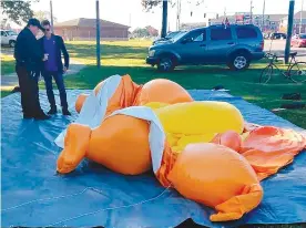  ?? The Tuscaloosa News via AP ?? ■ A responding officer and an unidentifi­ed man stand Saturday next to a Baby Trump balloon deflated by someone at Monnish Park. People were protesting President Donald Trump’s visit to an NCAA college football game between Louisiana State and Alabama playing nearby in Tuscaloosa, Ala., Saturday. The towering Baby Trump protest balloon was knifed and deflated by someone unhappy with its appearance during Trump’s trip to Alabama, organizers said.