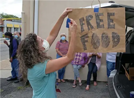  ??  ?? ‘MAKE FOOD AVAILABLE’: Tracy Sylven hangs a ‘Free Food’ sign before distributi­ng food to people in Mattapan on Saturday.