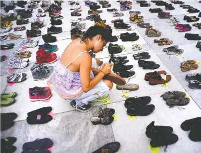  ?? AP FILE PHOTO BY RAMON ESPINOSA ?? A woman places one of the hundreds of shoes in memory of those killed by Hurricane Maria in front of the Puerto Rico Capitol, in San Juan in June.