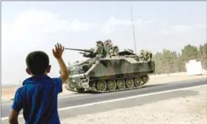  ??  ?? A Turkish boy waves to Turkish tank convoy driving into Syria from the border city of Karkamis in the southern region of Gaziantep.