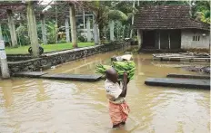  ?? AFP ?? A man carries a basket of bananas past houses immersed in flood waters in Kochi in Ernakulam district.