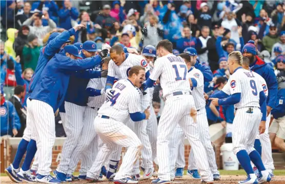  ??  ?? Shortstop Addison Russell is mobbed by teammates after hitting a walk- off three- run homer Wednesday. Kris Bryant had tied the score with a single two batters before. | AP