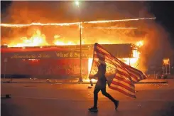  ?? JULIO CORTEZ/ASSOCIATED PRESS ?? A protester carries a U.S. flag upside down, a sign of distress, near a burning building Thursday in Minneapoli­s. The protests broke out over the death of George Floyd, a black man who died in police custody Monday.