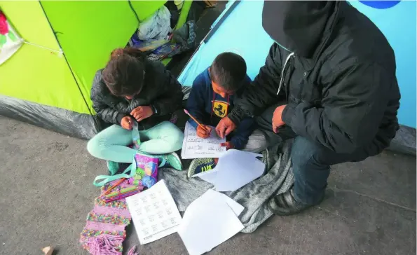  ?? REUTERS ?? Un solicitant­e de asilo ayuda a sus hijos a hacer sus deberes en un campo en Los Cerros (Tijuana)